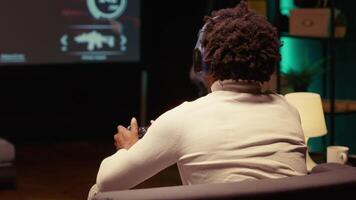 Close up shot of BIPOC man playing SF FPS videogame on widescreen smart TV, having fun in dark apartment room. Gamer competing in online multiplayer game, using headphones to chat with teammates video