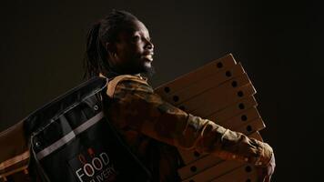 Takeout courier delivering huge pizza order on camera, carrying big stack of cardboard boxes as fast food meal. African american deliveryman bringing takeaway food, stylish trendy man. video