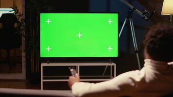 Man using remote to zap through films available on streaming services on mockup TV. Person having movie night in home theatre using isolated screen television set, relaxing on couch video