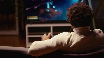 Man using cloud gaming service to play demanding science fiction videogame on large TV display. Gamer enjoying high quality graphics, streaming game online, handheld camera shot video