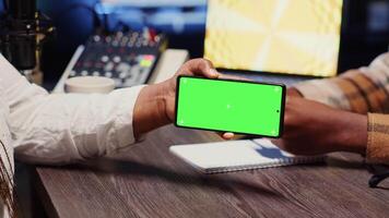 Man invited to podcast watching internet clips on green screen phone with host in apartment studio. Guest reacting to videos on mockup smartphone during online comedy show