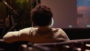 Afrikaanse Amerikaans Mens aan het kijken video Aan breedbeeld slim TV van fps in vaag lit leven kamer. speler aan het leren naar Speel spel door op zoek Bij internet gids Aan televisie Scherm
