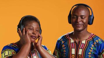 afrikansk amerikan partners dans på headsetet musik i studio, har roligt tillsammans med Häftigt häftig sånger. etnisk par håller på med skraj dansa rör sig och känsla avslappnad med hörlurar. video