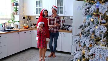 Happy family in santa hats with tiny house in cozy home with Christmas decor of festive white kitchen. Gift for New Year. Insurance, moving to new house, mortgage, rent and purchase real estate video
