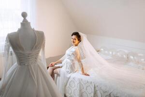 The bride in a silk suit with a veil poses in her room. Morning of the bride. Preparation. Wedding photography photo