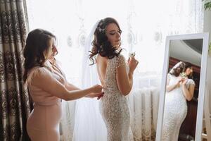 Morning of the bride. The bride's maid of honor helps the bride lace up her dress, fasten buttons on the dress or sleeves. Girlfriends help the bride fasten her dress photo