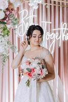 a brunette bride in a tiara poses with a bouquet of white and pink flowers. Beautiful hair and makeup. Spring wedding photo