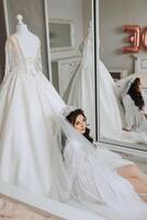 portrait of a luxurious bride in boudoir style near a mirror with reflection. Preparing the bride for the wedding in the morning in a white robe. photo