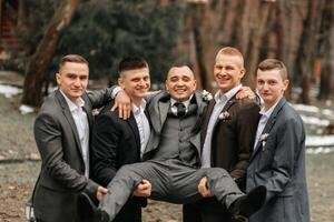 The groom and his friends are dressed in suits, fooling around in nature during a photo shoot. A group of men. Wedding in nature