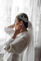 The bride in a silk suit and veil poses in her room. Morning of the bride. Preparation. Wedding photography photo