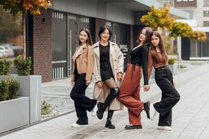 Group of smiling and happy teenage friends wearing casual clothes spending time together, posing and talking with each other near college building on autumn day. photo