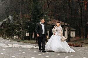 el novia y novio son caminando cerca el hotel y posando, contento y disfrutando el día, participación manos. un largo tren en el vestido. invierno Boda foto