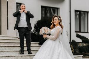 The bride and groom are walking near the hotel and posing, happy and enjoying the day, holding hands. A long train on the dress. Winter wedding photo