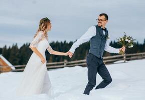 The bride and groom walk hand in hand against the background of a winter forest in the mountains. Snow. Couple walking to the mountain, side view. Winter wedding. photo