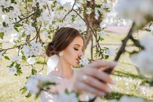un Pelirrojo novia poses en contra el antecedentes de un floreciente árbol. magnífico vestir con largo mangas, abierto busto. primavera Boda foto