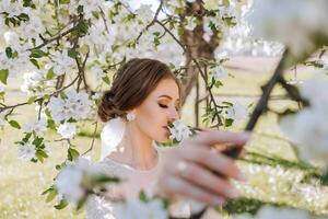 A red-haired bride poses against the background of a blooming tree. Magnificent dress with long sleeves, open bust. Spring wedding photo