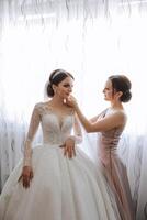 Morning of the bride. The bride's maid of honor helps the bride lace up her dress, fasten buttons on the dress or sleeves. Girlfriends help the bride fasten her dress photo