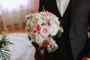 Stylish portrait of the groom with a bouquet of flowers. A man is preparing for a wedding ceremony in the morning. Groom's morning. Preparation for the groom's morning. Young and handsome groom. photo