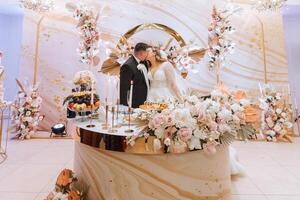 hermosa novia y novio celebrar su Boda a un fiesta. recién casados hacer un brindis a un contento casamiento, en pie a un comida mesa decorado con flores y seco flores foto