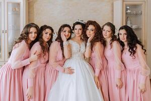 retrato de el novia con su amigos en el habitación. un morena novia en un largo blanco vestir y su amigos en rosado vestidos son sonriente y contento. joven chicas. foto