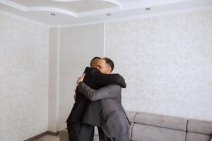 un padre abrazos su maduro hijo y ayuda él preparar para el Boda ceremonia. calentar y sincero relaciones Entre un padre y un adulto hijo. un emocional momento a un Boda foto