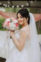 a brunette bride in a tiara poses with a bouquet of white and pink flowers. Beautiful hair and makeup. Spring wedding photo