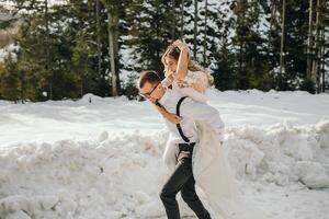 The bride and groom are running along a snowy road against the background of a pine forest and beautiful contrast sunlight. Side view. Winter wedding. Place for logo. photo