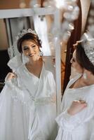 portrait of a luxurious bride in boudoir style near a mirror with reflection. Preparing the bride for the wedding in the morning in a white robe. photo