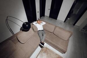 Satisfied handsome guy relaxing on sofa in hotel, resting, looking at camera, hands behind head, smiling happily. Relaxation, self care, enjoy life concept photo