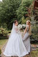 Group portrait of the bride and bridesmaids. A bride in a wedding dress and a bridesmaid in a silver dress hold a stylish bouquet on their wedding day. photo