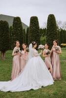 grupo retrato de el novia y damas de honor novia en un Boda vestir y damas de honor en rosado o polvo vestidos y participación elegante ramos de flores en el Boda día. foto