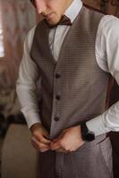 The groom fastens a button on his vest at the groom's morning gatherings. Groom wedding preparation. photo