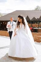 A beautiful young bride, in a summer park, walks ahead of her groom. Beautiful wedding white dress. Walks in the park. A happy and loving couple. photo