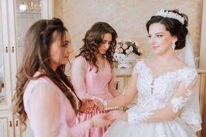 A friend helps the bride fasten her dress. A woman helps her friend fasten the buttons on the back of her wedding dress. The morning of the bride, the creation of a family, an important event. photo