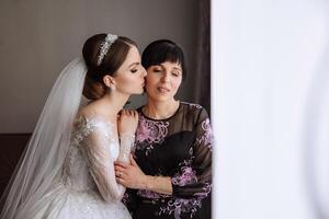 A beautiful and happy mother and her daughter, the bride, are standing next to each other. The best day for parents. Tender moments at the wedding. photo