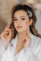 Morning of the bride before the wedding. A beautiful young woman with a veil and a beautiful hairstyle in a white robe in a room with a wonderful interior. Natural beauty and professional makeup. photo