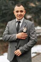 The groom in a gray suit poses during a walk in the forest. Business style. Winter wedding. photo