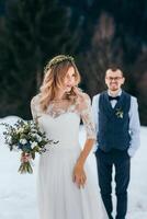 winter wedding in the mountains. The bride is waiting for the groom. A beautiful bride in a white dress and a bouquet of flowers in her hands. A modern winter wedding photo