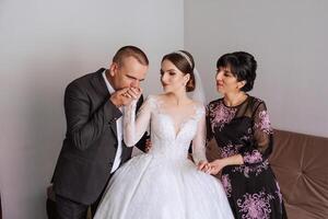 Happy parents hold the hands of the bride who is getting married and support her, wearing a wedding dress and a long veil. photo