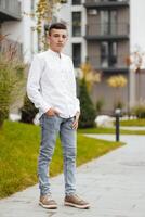 Vertical close-up portrait of a teenager in casual clothes. Happy smiling teenager in autumn park in sunlight. A beautiful child looks at the camera in nature. photo