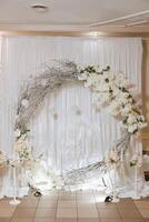 un hermosamente decorado sitio para el Boda ceremonia de el novia y novio en un moderno estilo. Boda arco hecho de blanco Fresco flores anillo tipo. foto