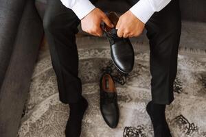 un elegante hombre usa negro cuero formal zapatos. atadura zapatos. negocio hombre atadura cordones de los zapatos en el piso. arriba cerca el novio es preparando para el boda. foto