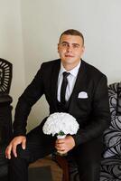 Stylish portrait of the groom with a bouquet of flowers. A man is preparing for a wedding ceremony in the morning. Groom's morning. Preparation for the groom's morning. Young and handsome groom. photo