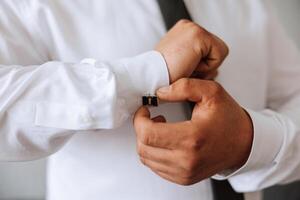 handsome business man buttoning shirt sleeves at home. The groom is preparing for the wedding. Close-up photo. photo