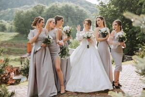 Group portrait of the bride and bridesmaids. A bride in a wedding dress and bridesmaids in silver dresses hold stylish bouquets on their wedding day. photo