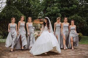 Group portrait of the bride and bridesmaids. A bride in a wedding dress and bridesmaids in silver dresses hold stylish bouquets on their wedding day. photo