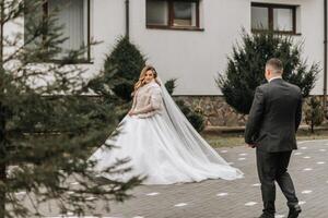 The bride and groom are walking near the hotel and posing, happy and enjoying the day, holding hands. A long train on the dress. Winter wedding photo