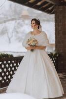 Happy bride in a beautiful dress against the background of snowy mountains. Winter wedding. Portrait of a beautiful bride in a white fur coat and wedding dress photo