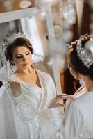 portrait of a luxurious bride in boudoir style near a mirror with reflection. Preparing the bride for the wedding in the morning in a white robe. photo