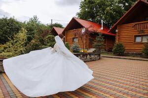 A red-haired bride is circling in her wedding dress, against the background of mountains and wooden houses. Magnificent dress with long sleeves, open bust. photo